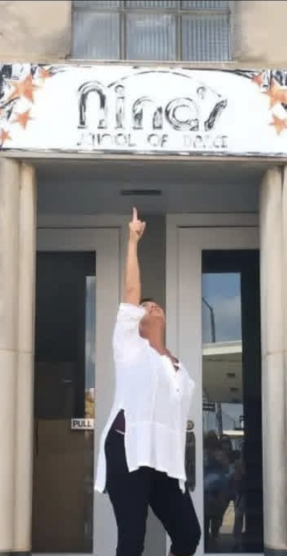 Nina Wheeler striking a pose beneath the sign of Nina's School of Dance